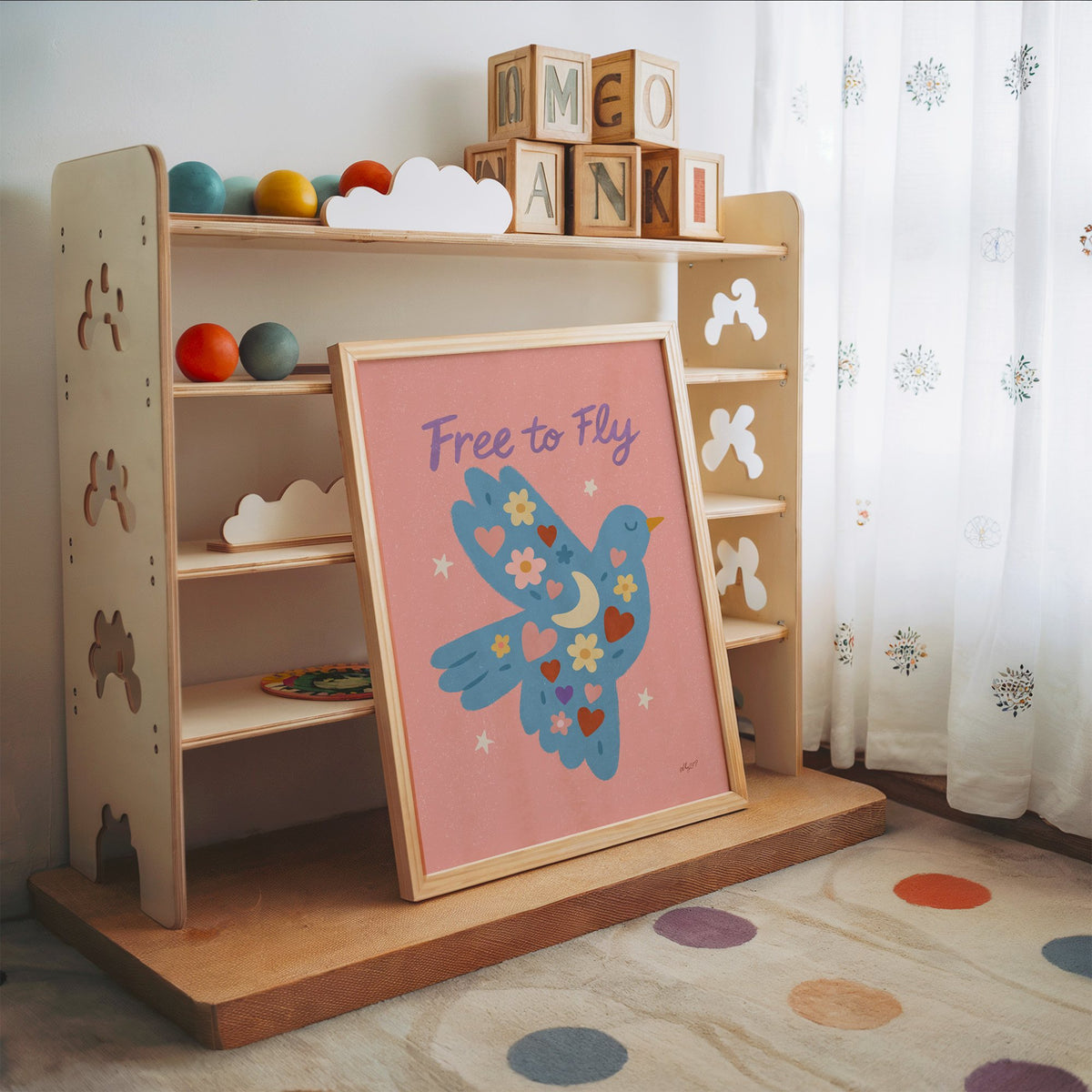Folk blue bird free to fly nursery print in an oak frame leaning on a toy shelf with wooden letter blocks