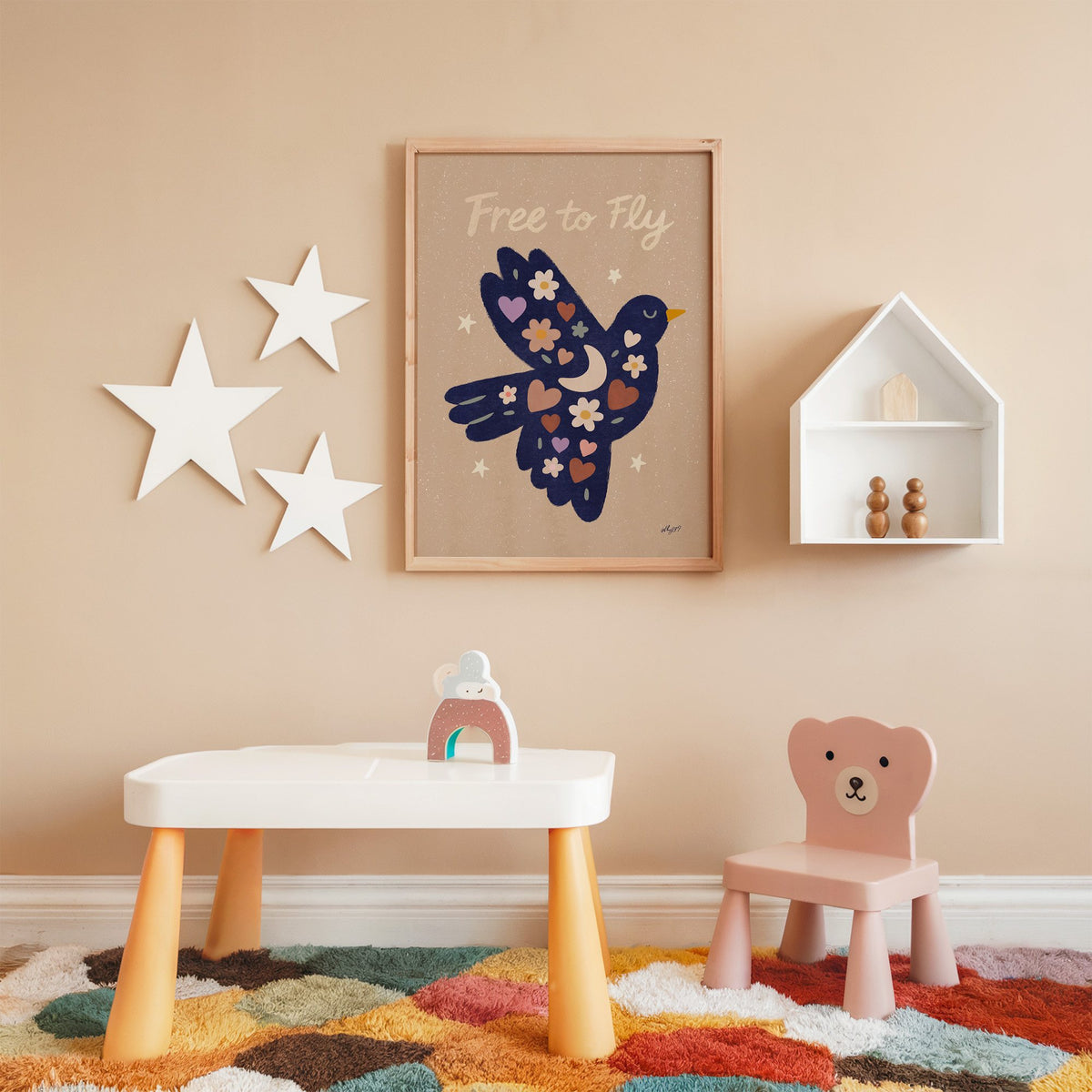 Navy folk bird free to fly nursery print in an oak frame on a peach wall above a kids table with wall stars