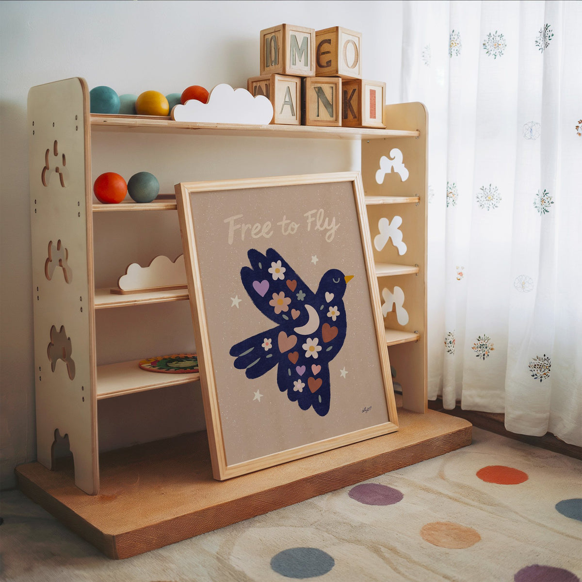 Navy folk bird free to fly nursery print in an oak frame leaning on a toy shelf with wooden letter blocks