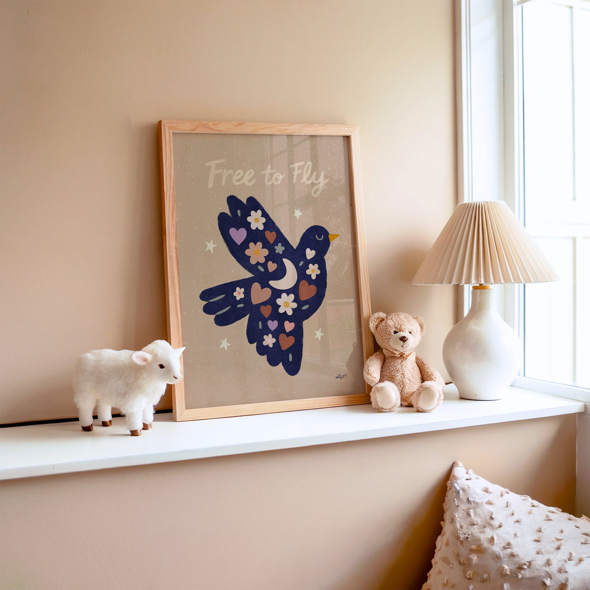 Navy folk bird free to fly nursery print in an oak frame on a window ledge with a toy lamb and teddy