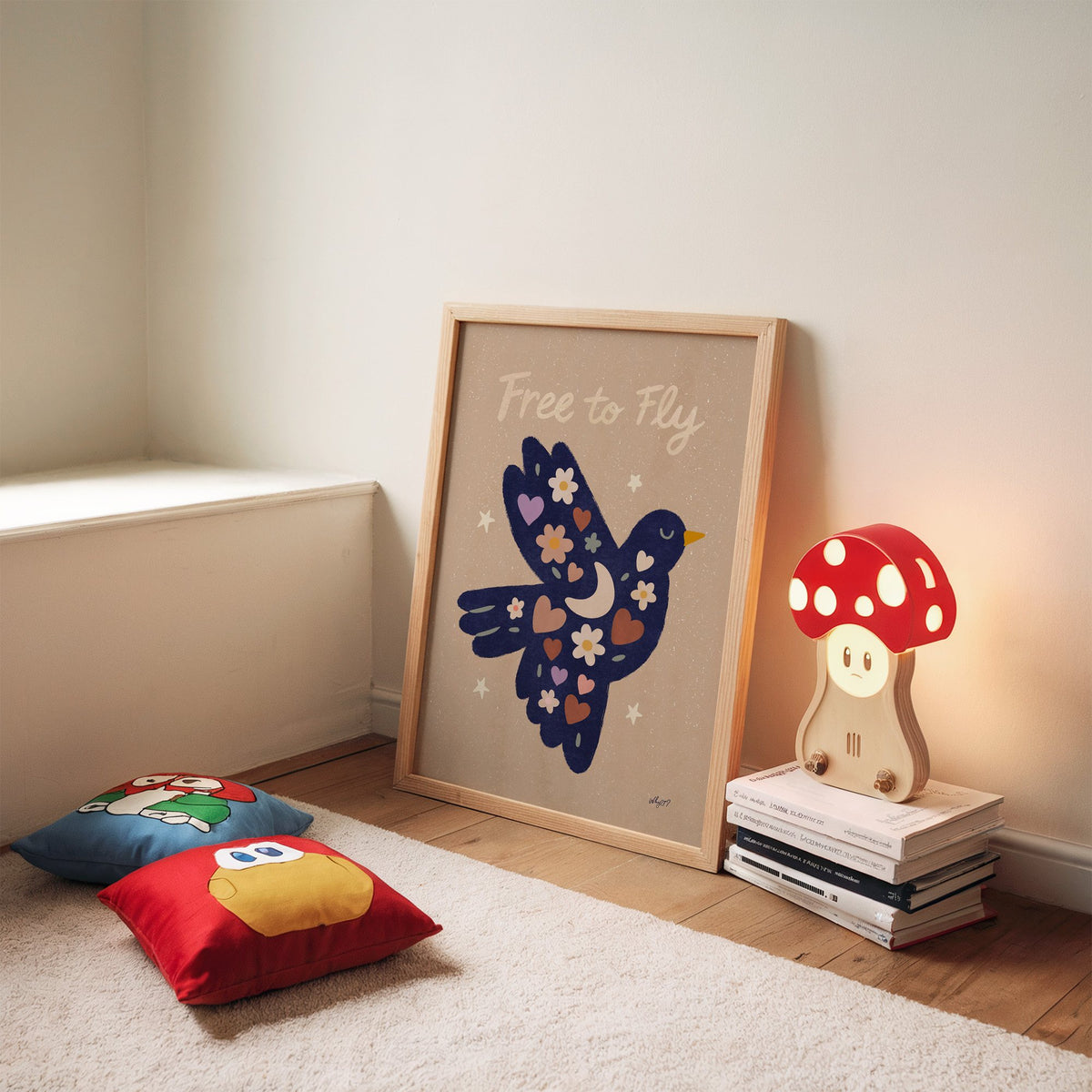 Navy folk bird free to fly nursery print in an oak frame leaning on a rug beside a mushroom lamp and floor cushions