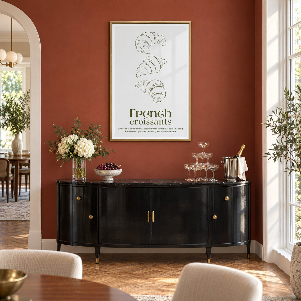 French croissants olive line print in a brass frame on a terracotta wall above a black buffet with a champagne tower