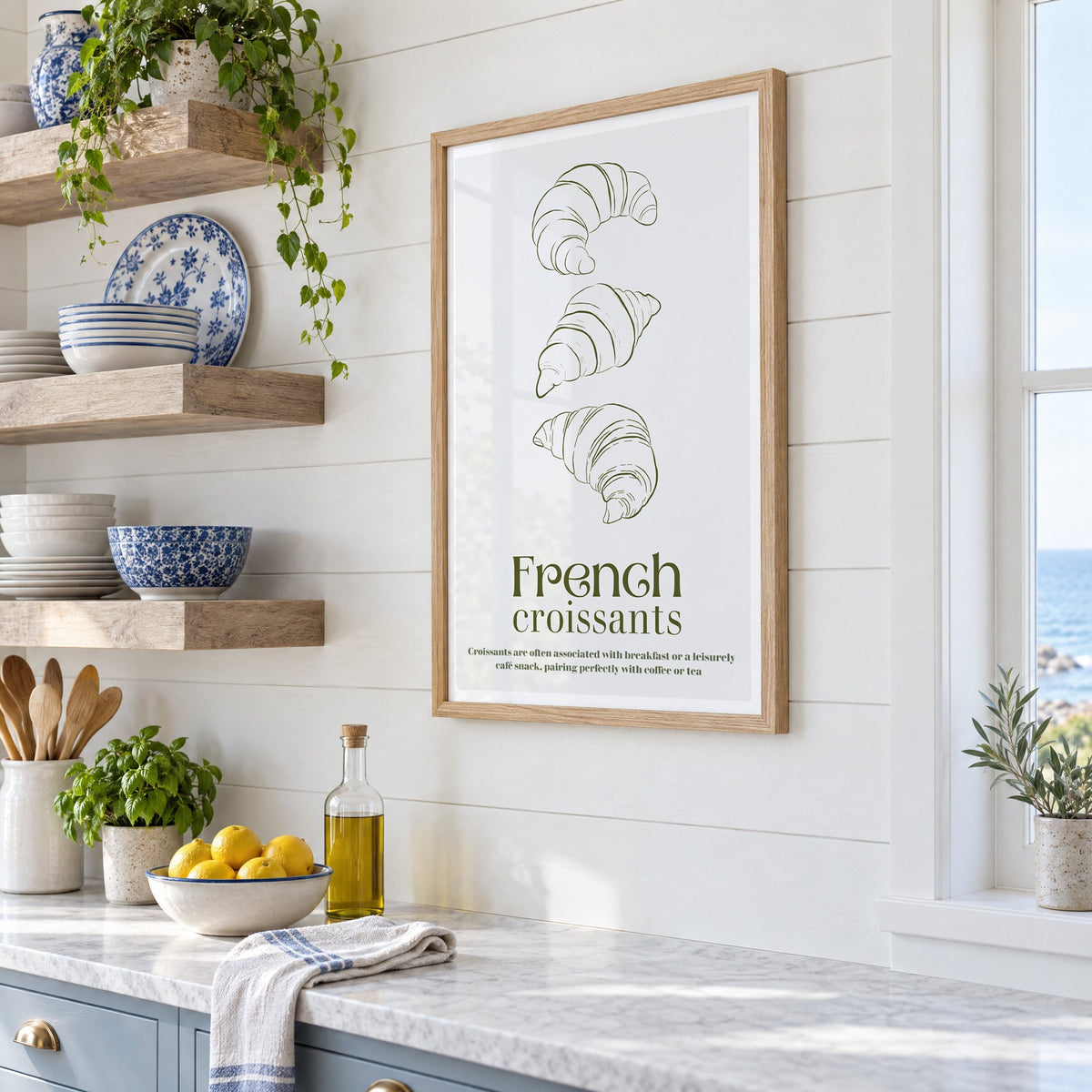 French croissants olive line print in an oak frame in a white coastal kitchen beside blue and white plates