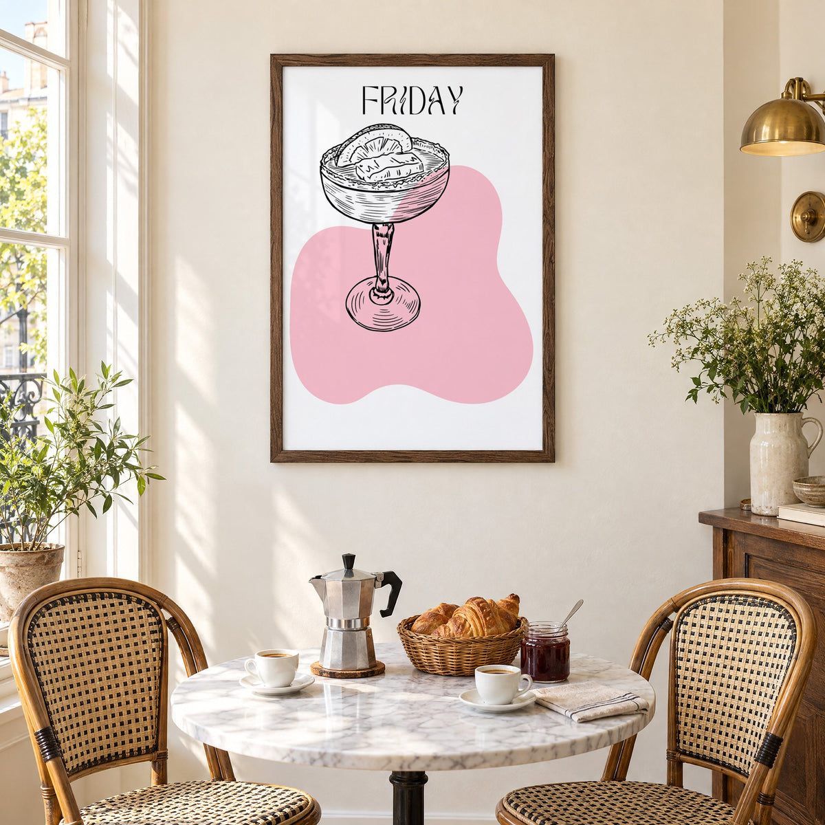FRIDAY engraved coupe cocktail pink blob print in a walnut frame above a marble bistro table with croissants and rattan chairs