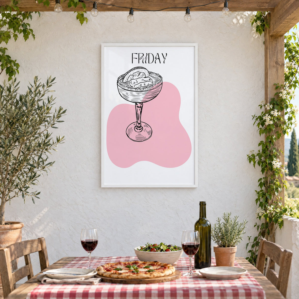FRIDAY engraved coupe cocktail pink blob print in a white frame on a stucco wall above a checked-cloth table with pizza and red wine