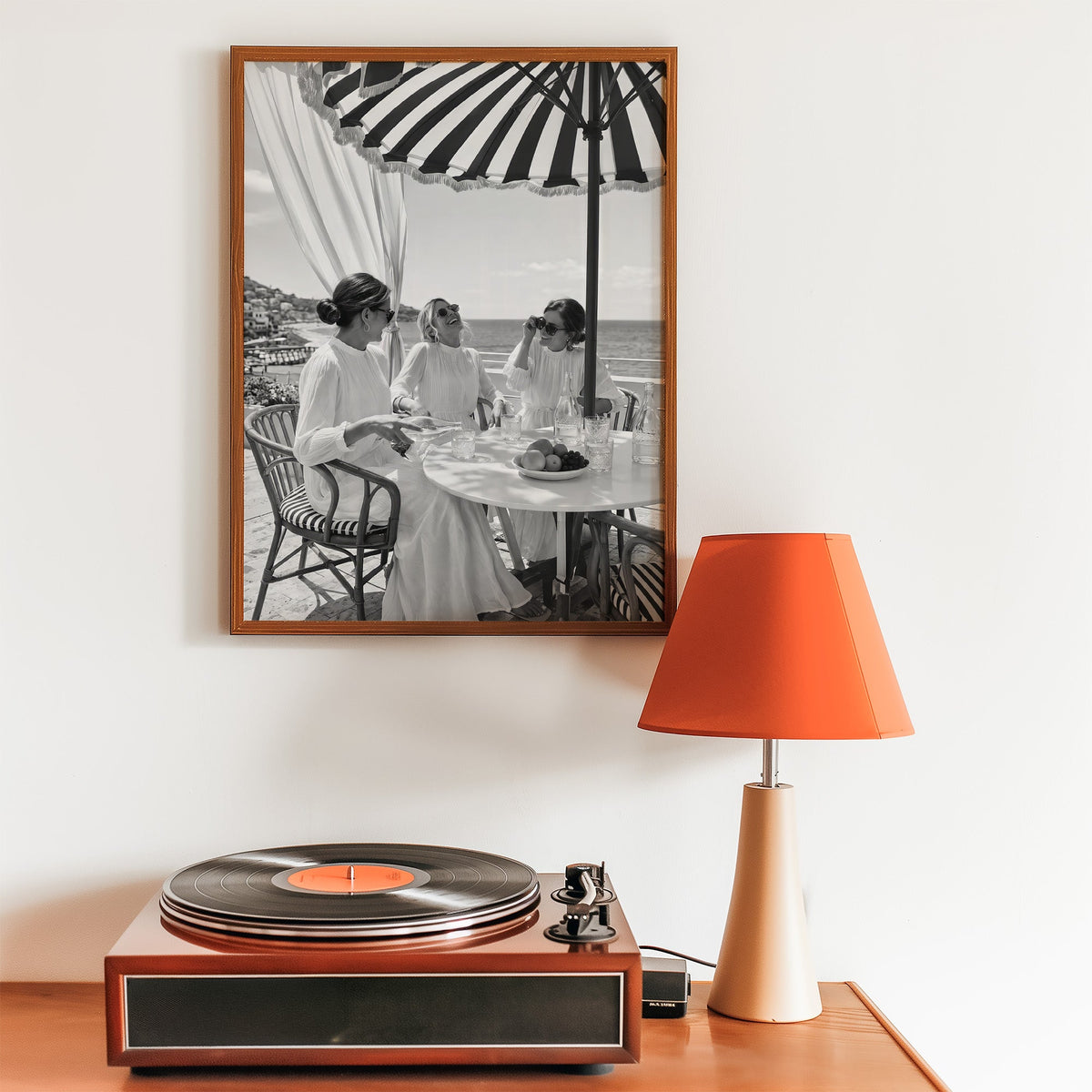 Three friends lunching under a striped umbrella print in a walnut frame above a record player and orange lamp