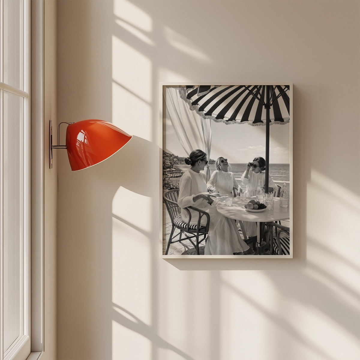 Three friends lunching under a striped umbrella print in a white frame on a sunlit wall beside a red sconce