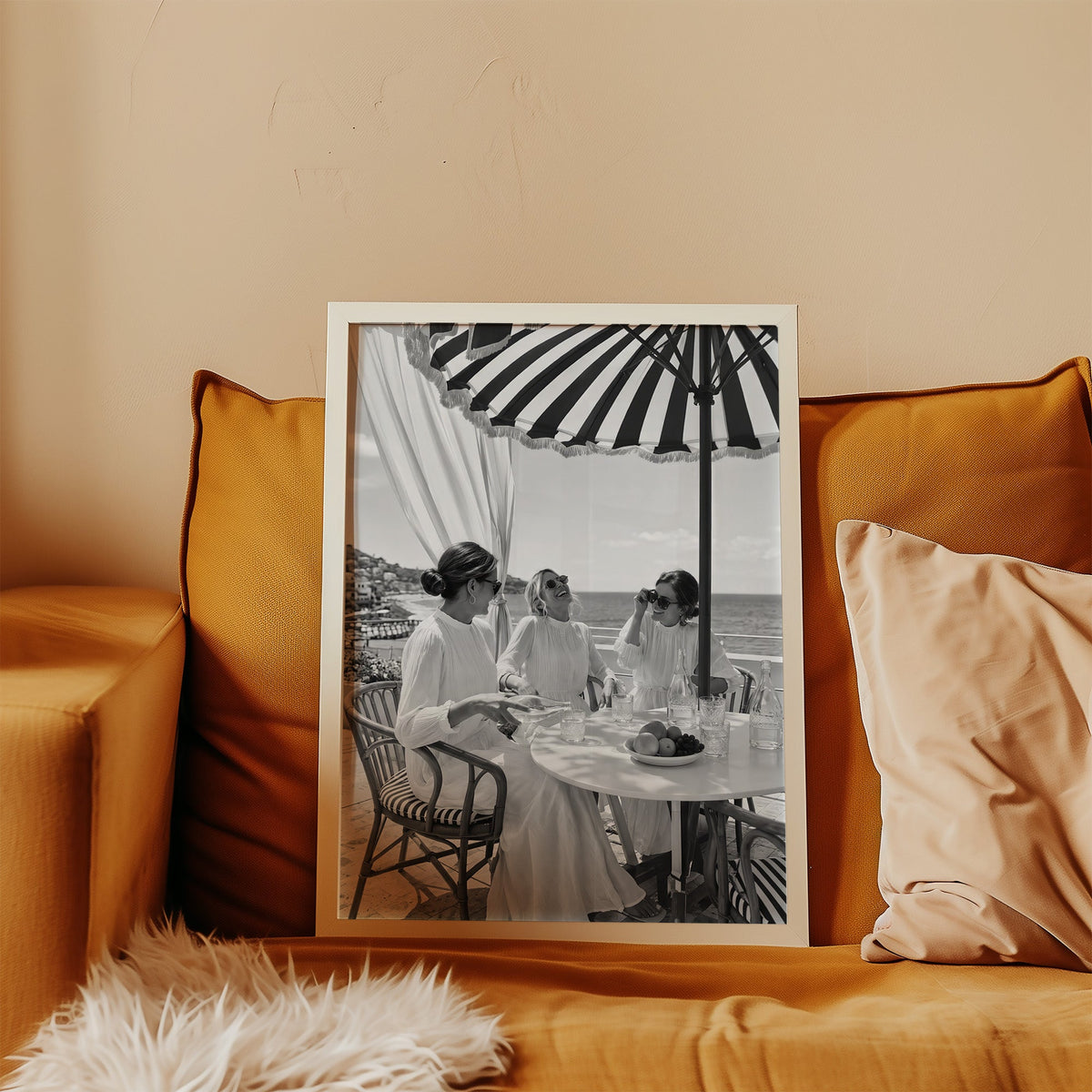 Three friends lunching under a striped umbrella print in a white frame leaning on a mustard velvet sofa