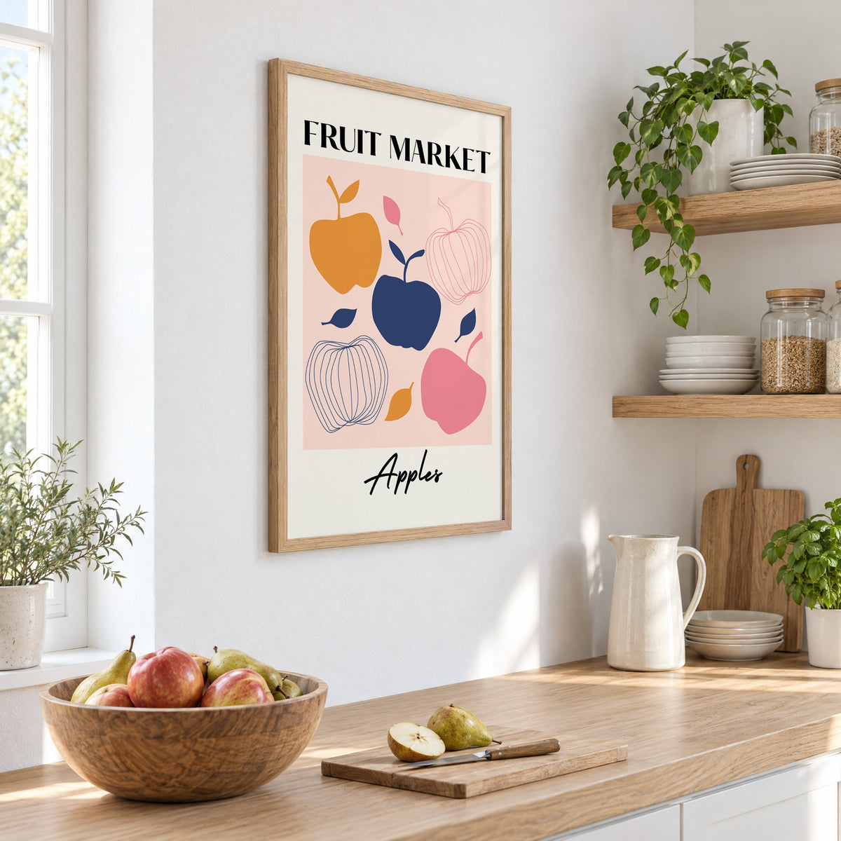 FRUIT MARKET Apples cut-paper print in an oak frame on a white kitchen wall above a counter with apples and pears, seen at an angle
