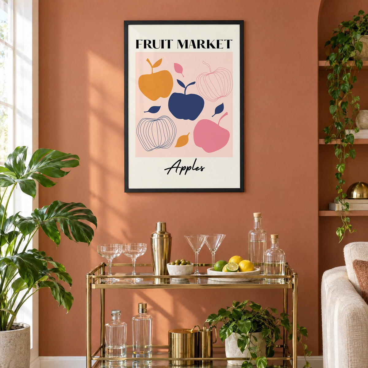 FRUIT MARKET Apples cut-paper print in a black frame on a terracotta wall above a brass bar cart with coupes and citrus