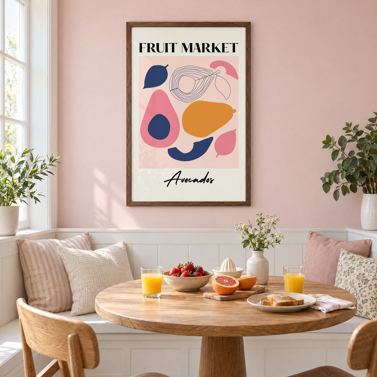 FRUIT MARKET Avocados cut-paper print in a walnut frame on a pastel pink wall above a breakfast nook with strawberries and orange juice