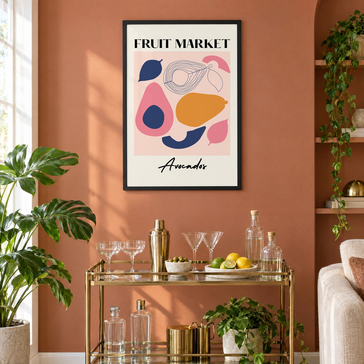 FRUIT MARKET Avocados cut-paper print in a black frame on a terracotta wall above a brass bar cart with coupes and citrus