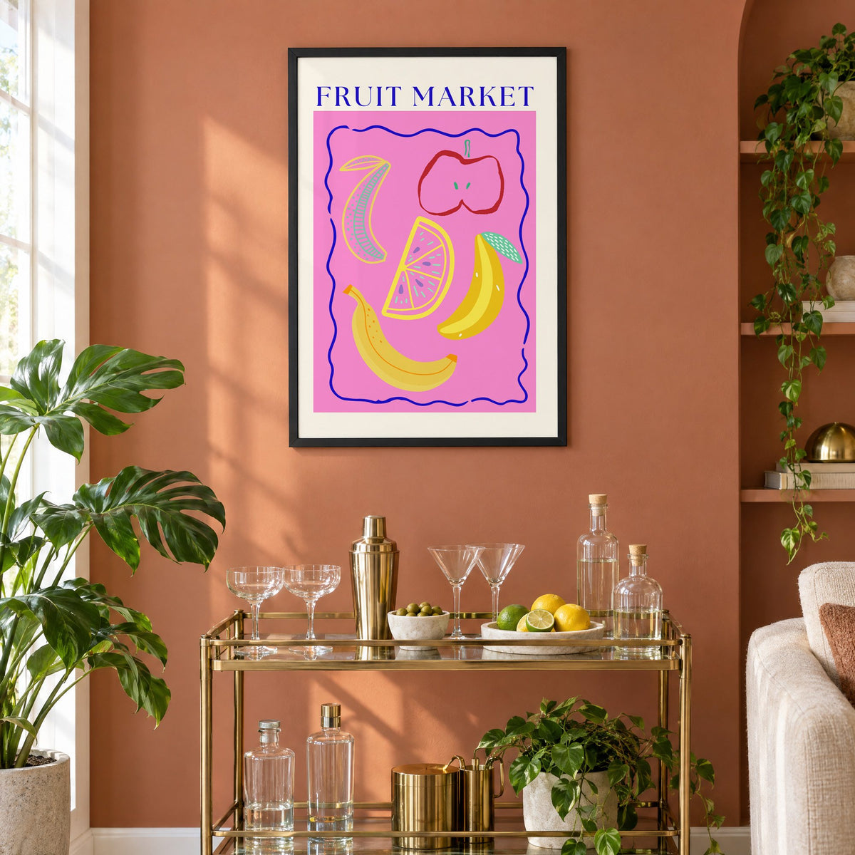 FRUIT MARKET bananas, apple and citrus print in a black frame on a terracotta wall above a brass bar cart with coupes and citrus