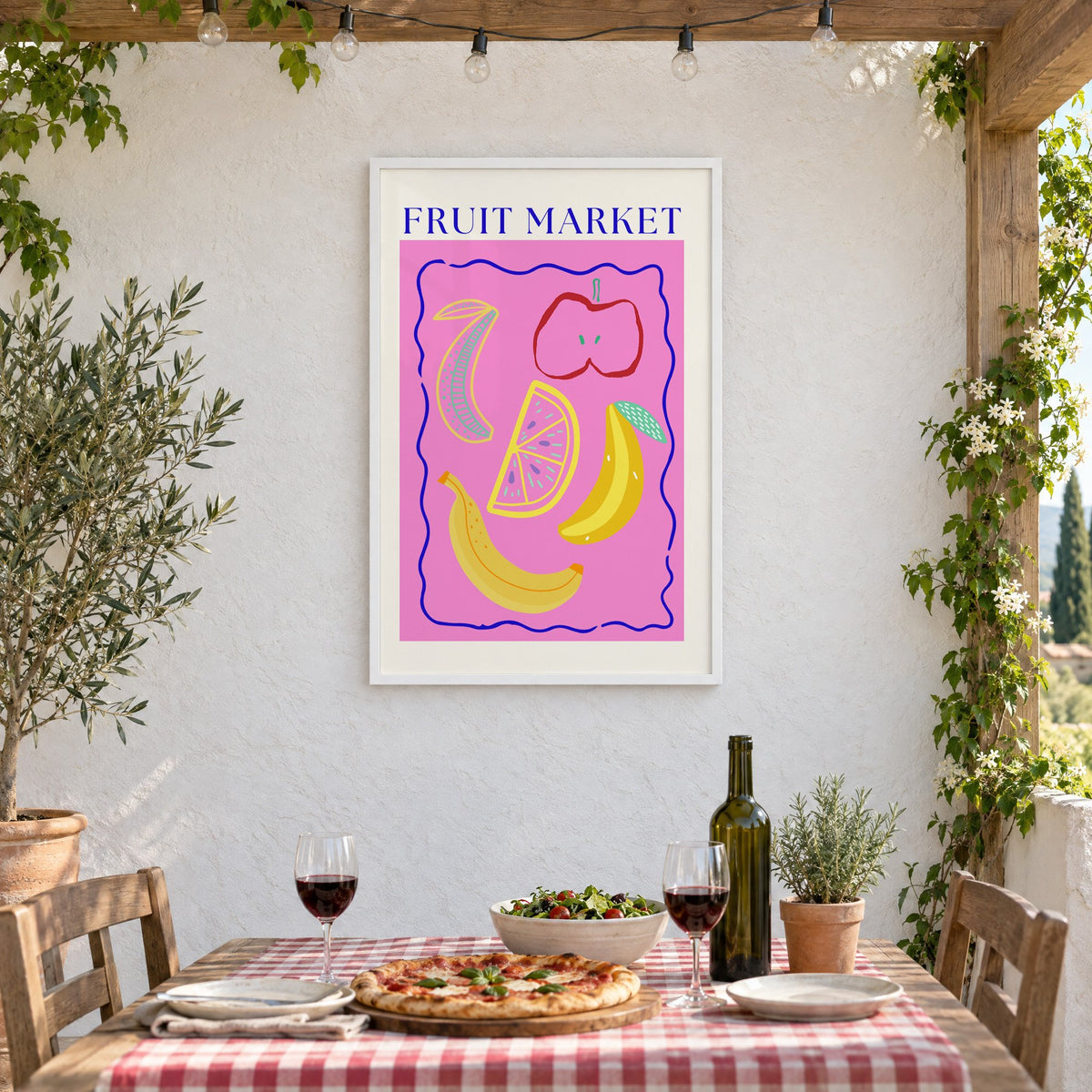 FRUIT MARKET bananas, apple and citrus print in a white frame on a stucco wall above a checked-cloth table with pizza and red wine