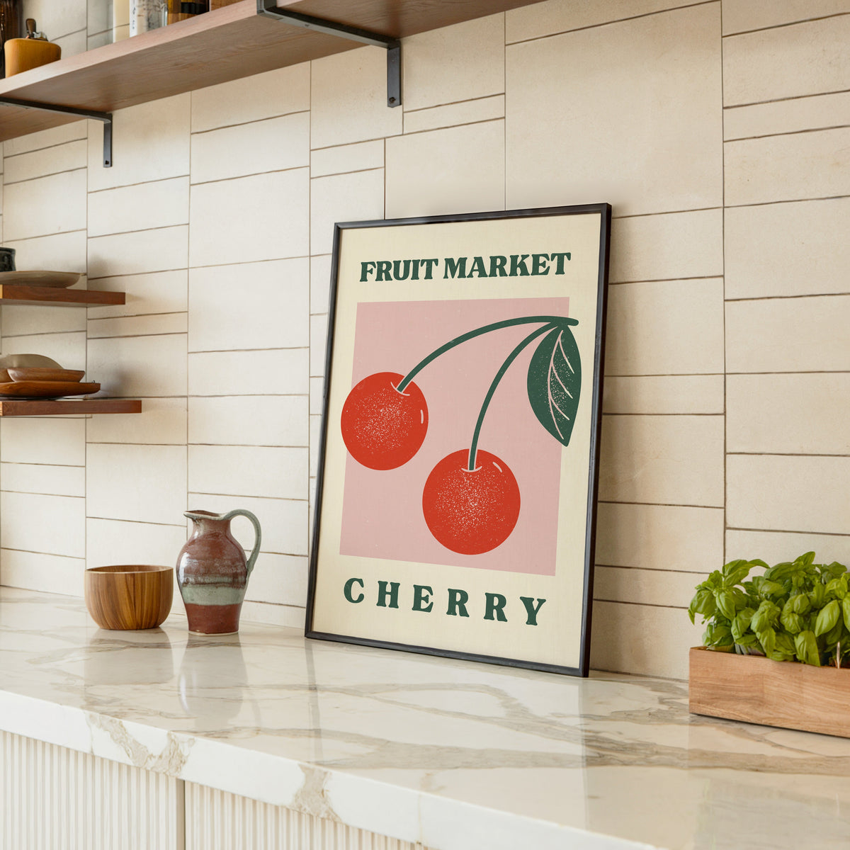 Fruit Market cherry print in a black frame leaning on a marble counter in a tiled kitchen