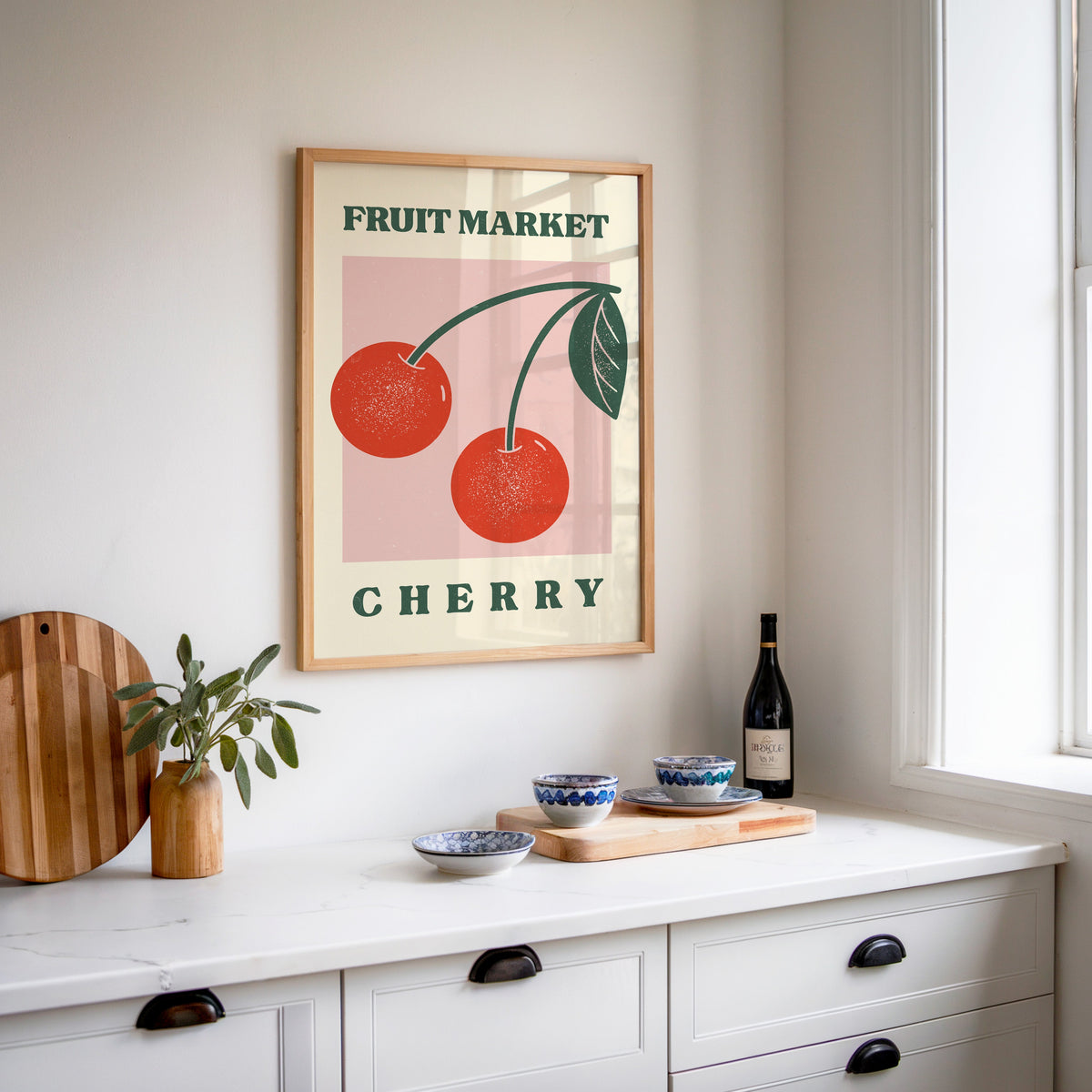 Fruit Market cherry print in an oak frame above a white sideboard with a bottle of wine