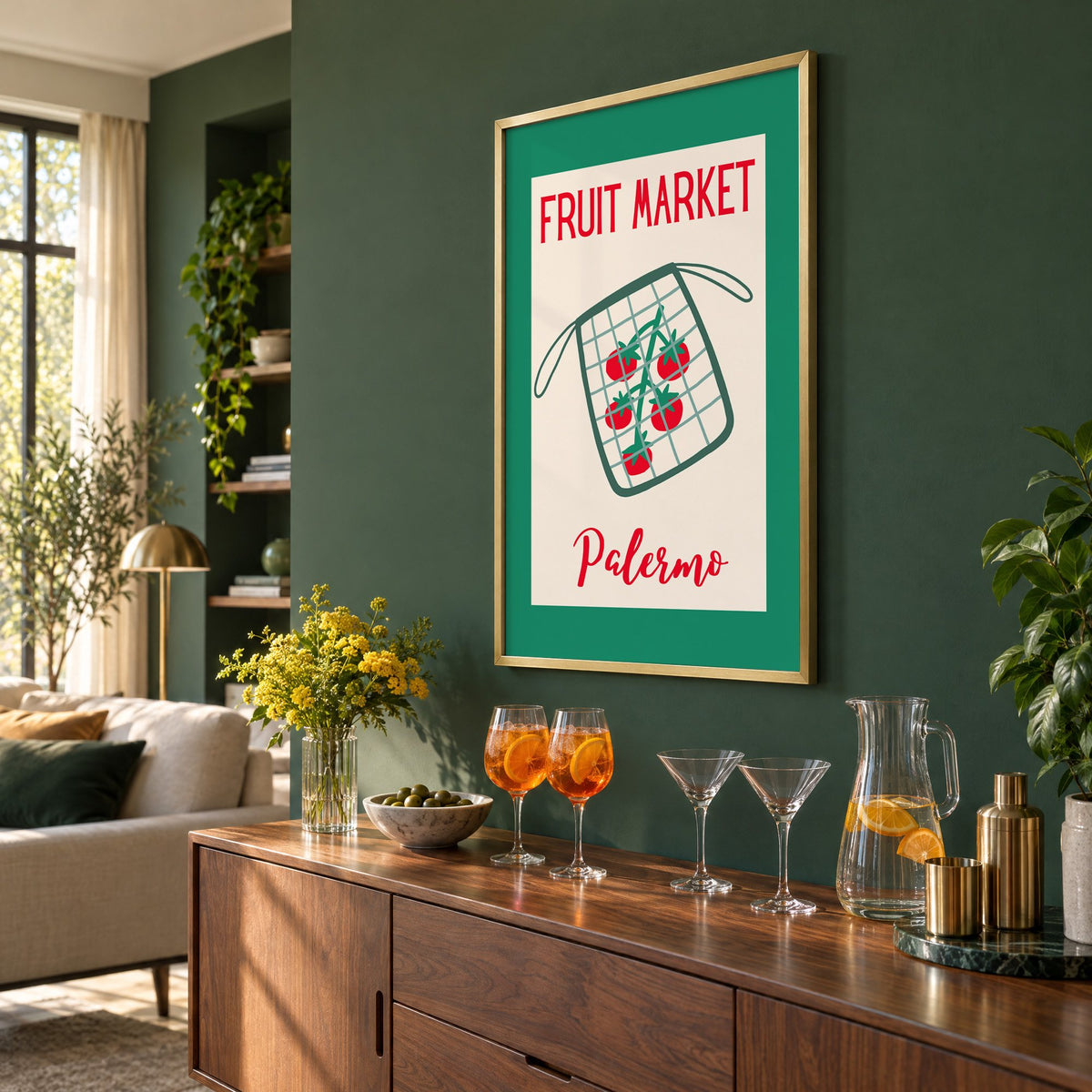 FRUIT MARKET Palermo tomato net bag print in a brass frame on a bottle green wall above a sideboard with spritz and martini glasses, seen at an angle