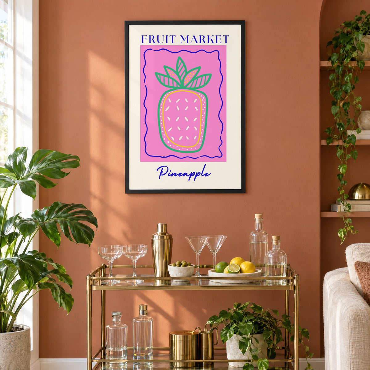 FRUIT MARKET Pineapple pink wavy frame print in a black frame on a terracotta wall above a brass bar cart with coupes and citrus