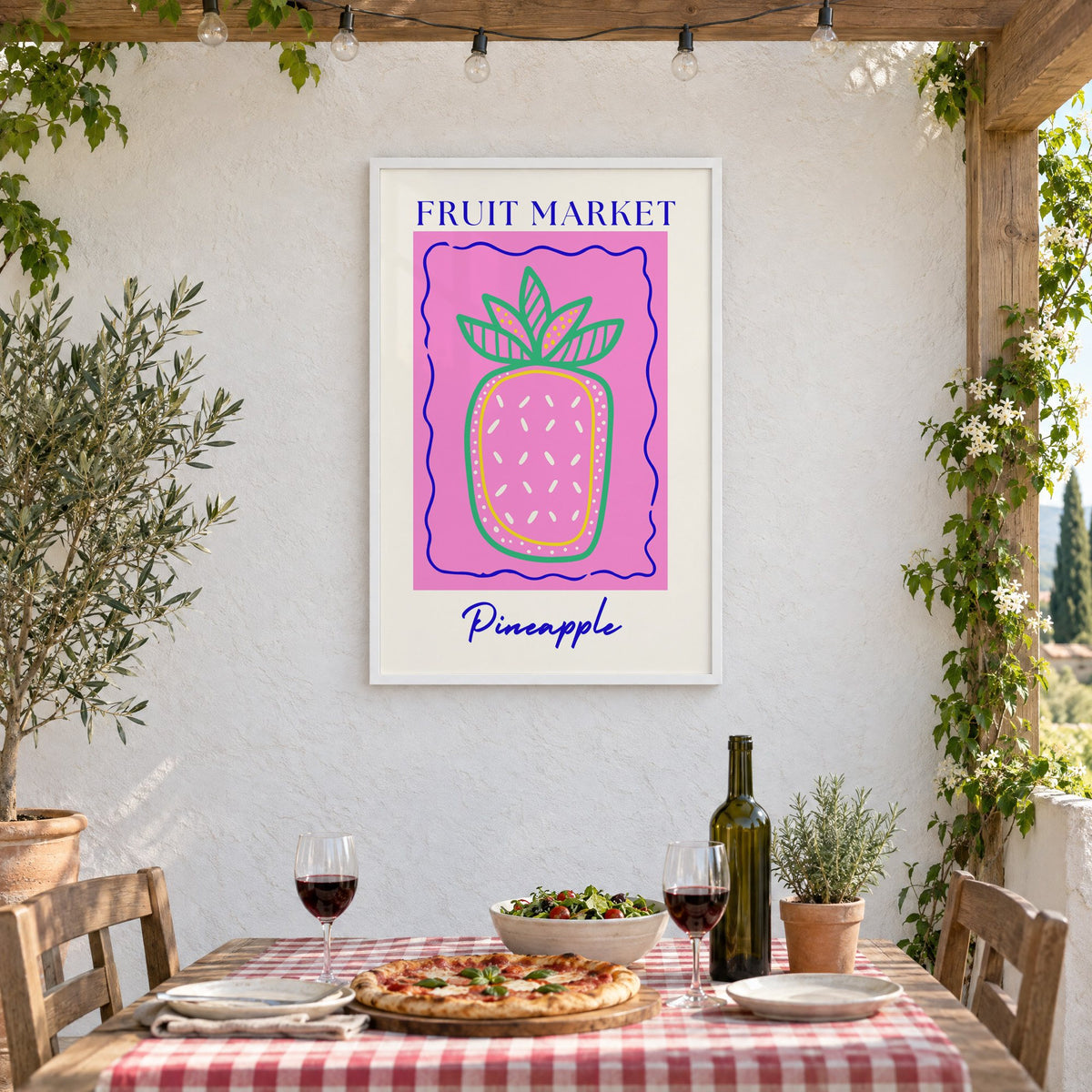 FRUIT MARKET Pineapple pink wavy frame print in a white frame on a stucco wall above a checked-cloth table with pizza and red wine