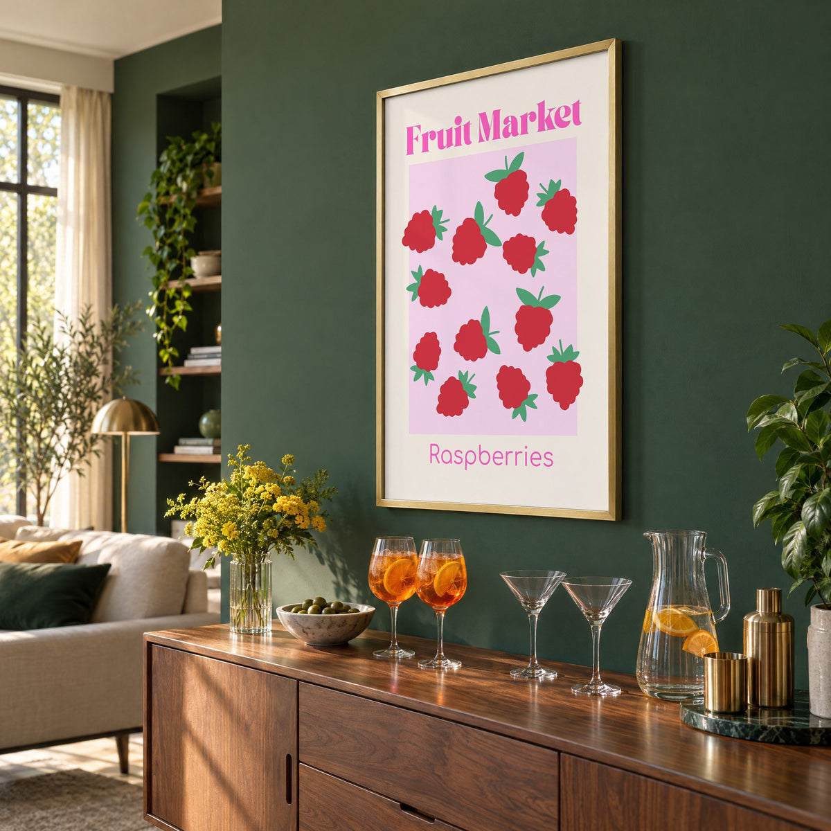Fruit Market Raspberries pink panel print in a brass frame on a bottle green wall above a sideboard with spritz and martini glasses, seen at an angle