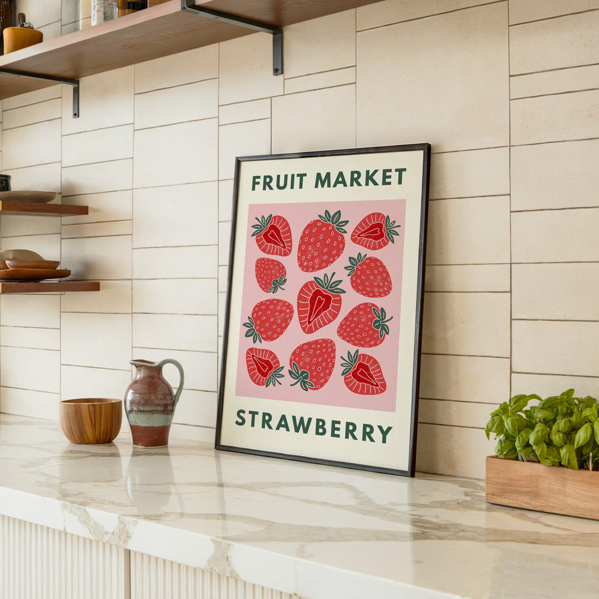 Fruit Market strawberry print in a black frame leaning on a marble counter in a tiled kitchen