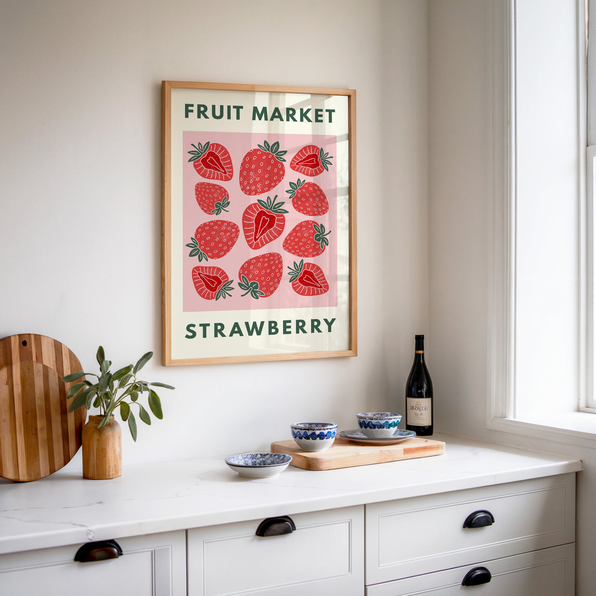 Fruit Market strawberry print in an oak frame above a white sideboard with a bottle of wine