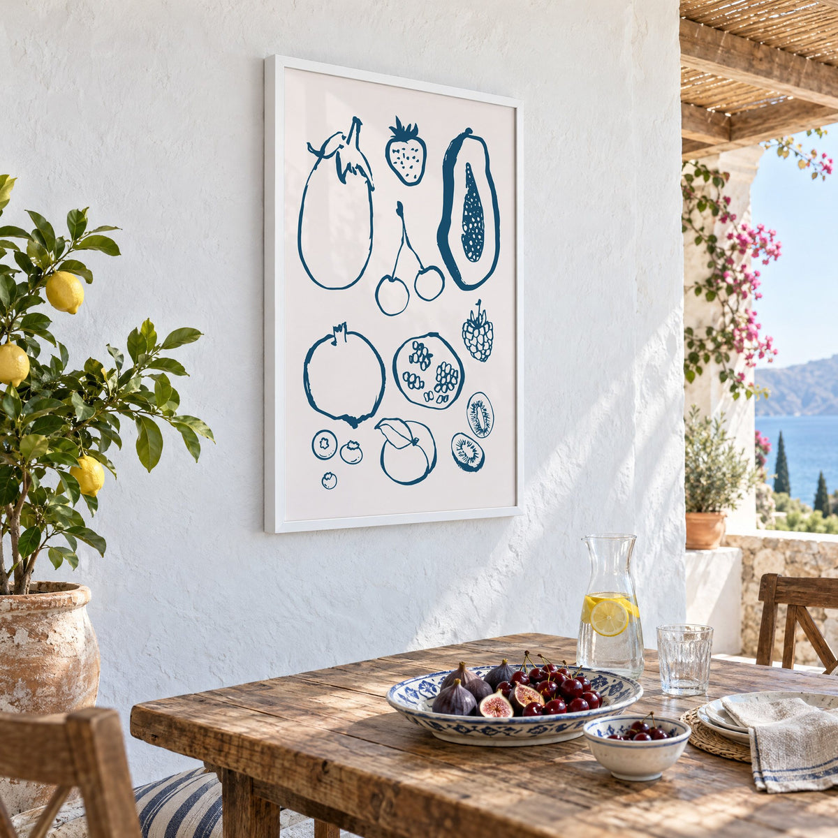 petrol blue ink fruit sketch pattern print in a white frame on a whitewashed terrace wall above a lunch table with figs and cherries, seen at an angle
