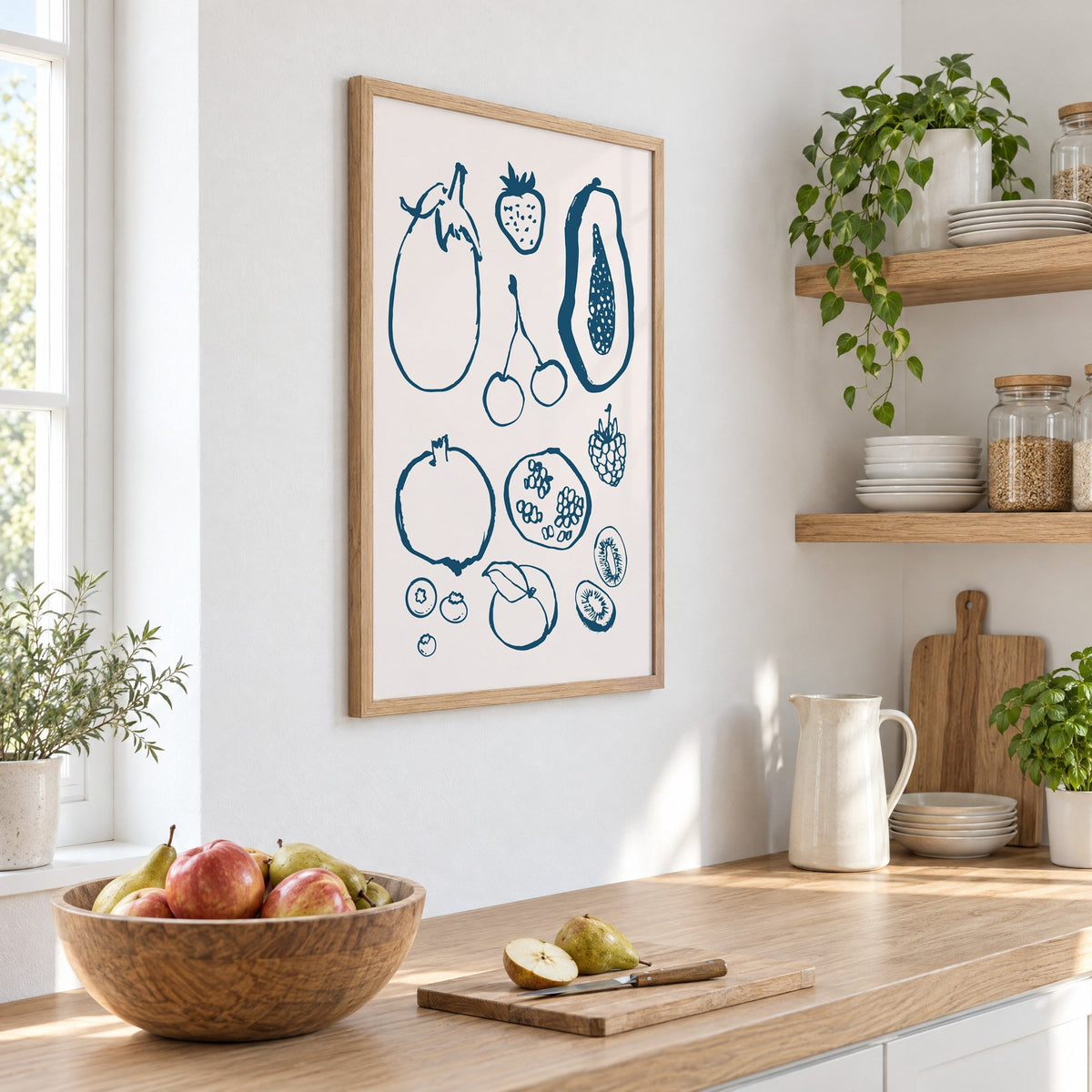 petrol blue ink fruit sketch pattern print in an oak frame on a white kitchen wall above a counter with apples and pears, seen at an angle