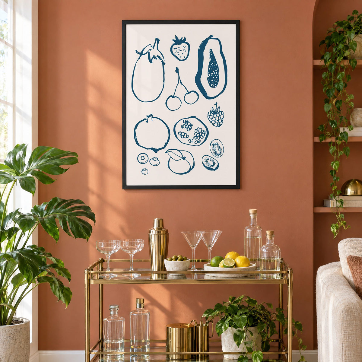 petrol blue ink fruit sketch pattern print in a black frame on a terracotta wall above a brass bar cart with coupes and citrus
