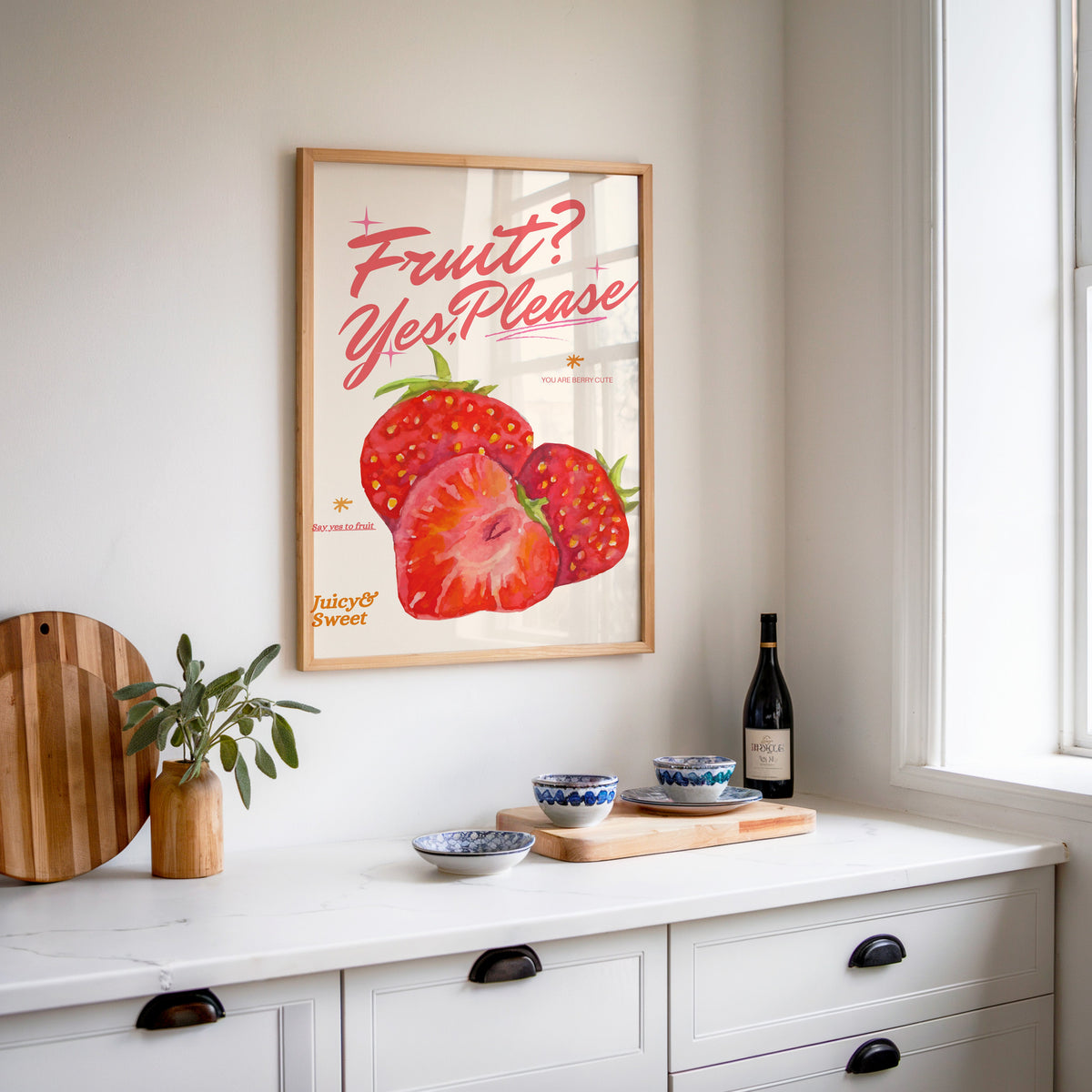 Fruit Yes Please strawberries print in an oak frame above a white kitchen sideboard with a wine bottle and wooden board