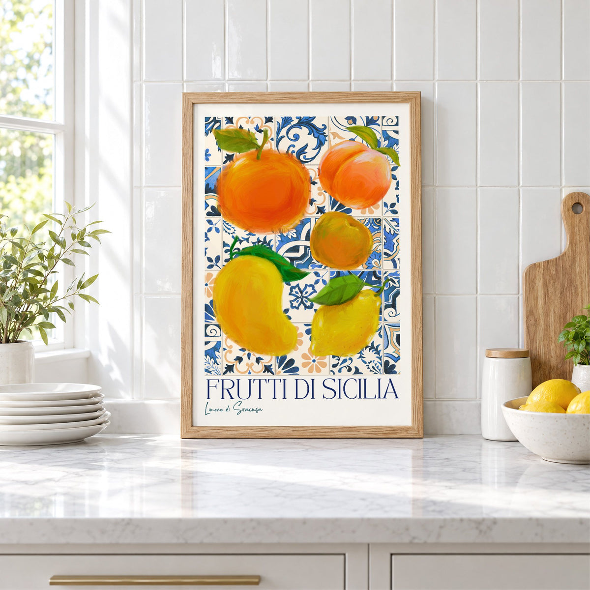 Frutti di Sicilia blue tile fruit print in an oak frame leaning on a marble counter by white tiles and lemons