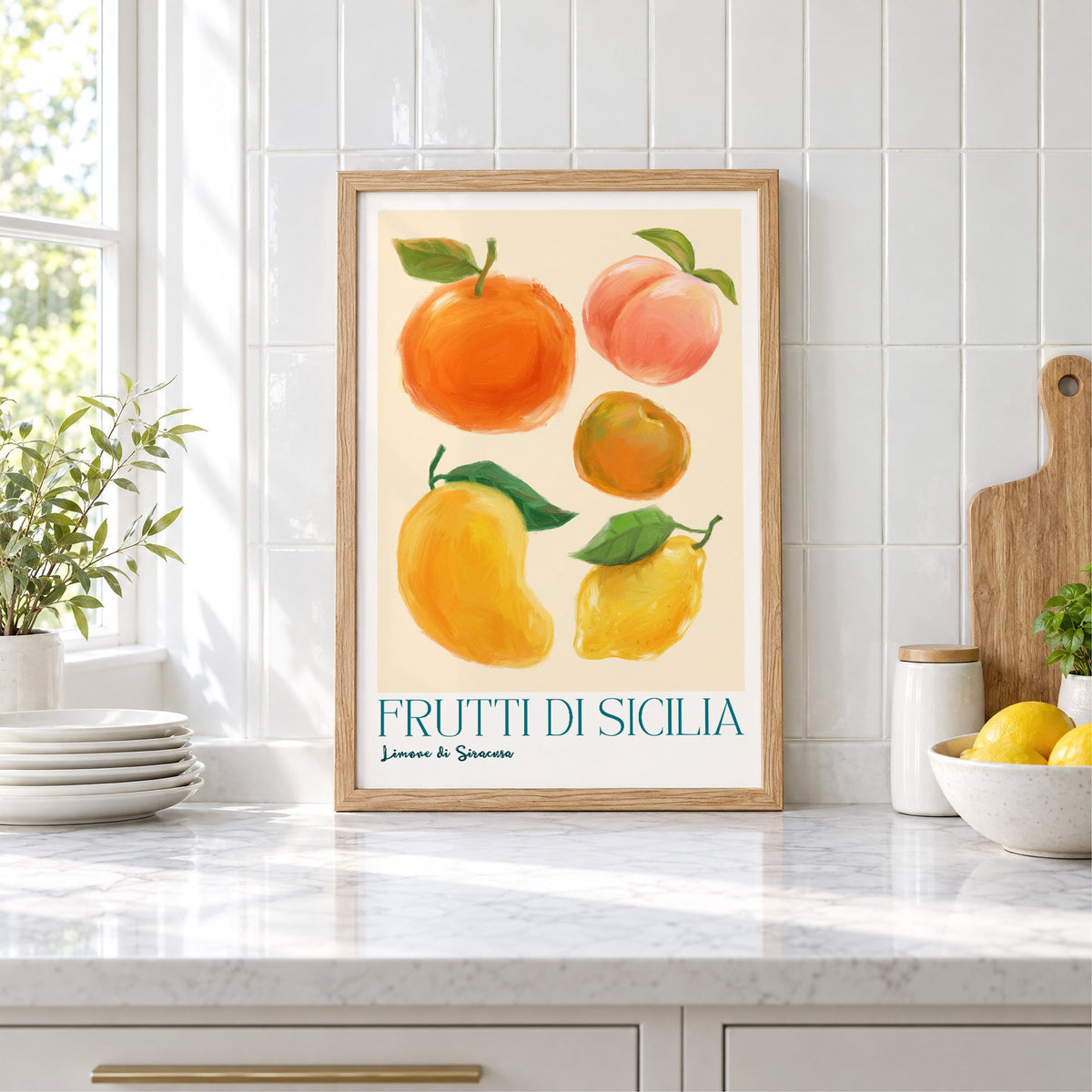 Frutti di Sicilia cream painted fruit print in an oak frame leaning on a marble counter by white tiles and lemons