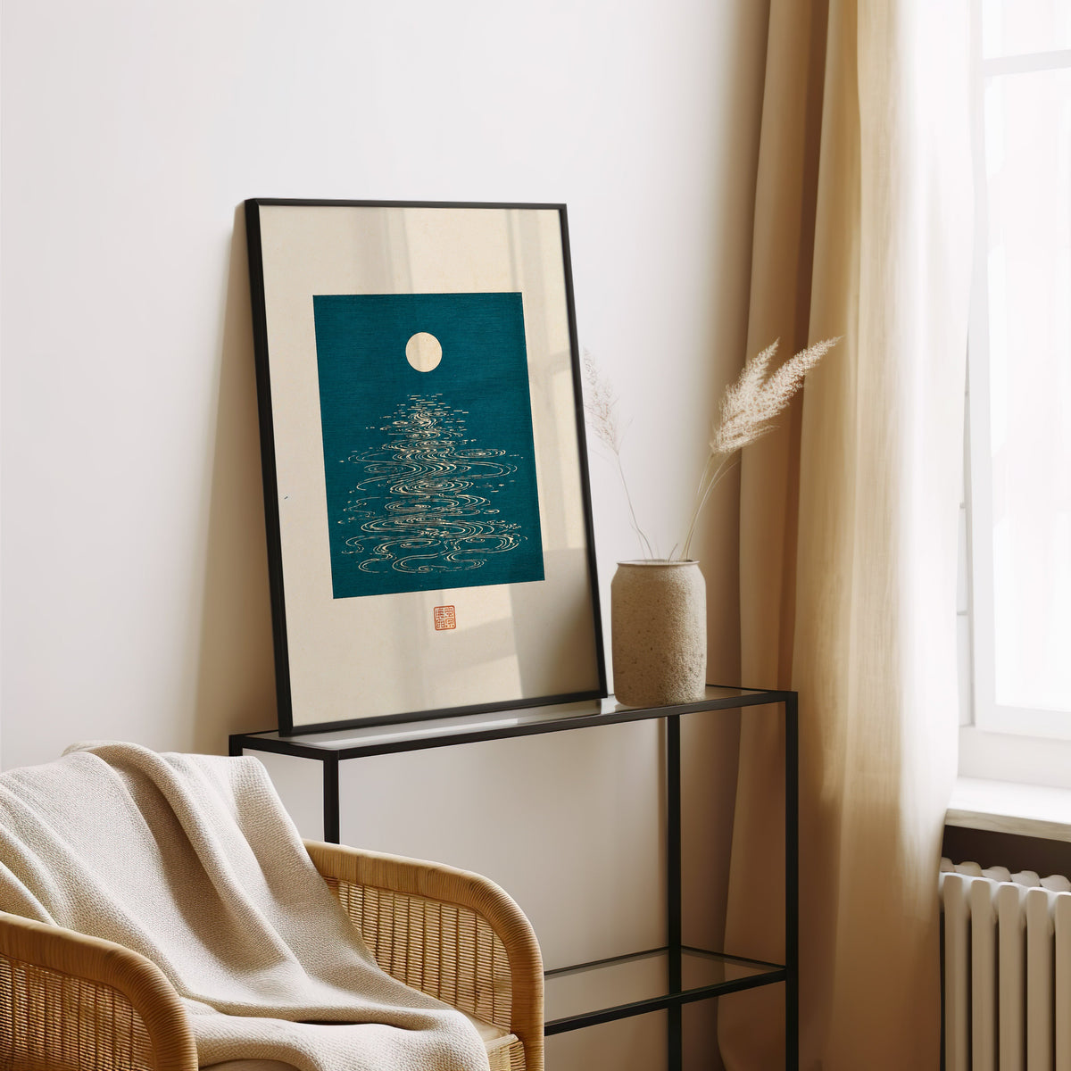 full moon over teal water print in a black frame leaning on a glass console beside pampas grass