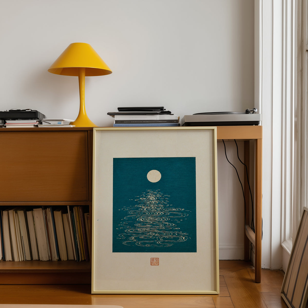 full moon over teal water print shown in a gold frame leaning under a teak desk with a yellow lamp