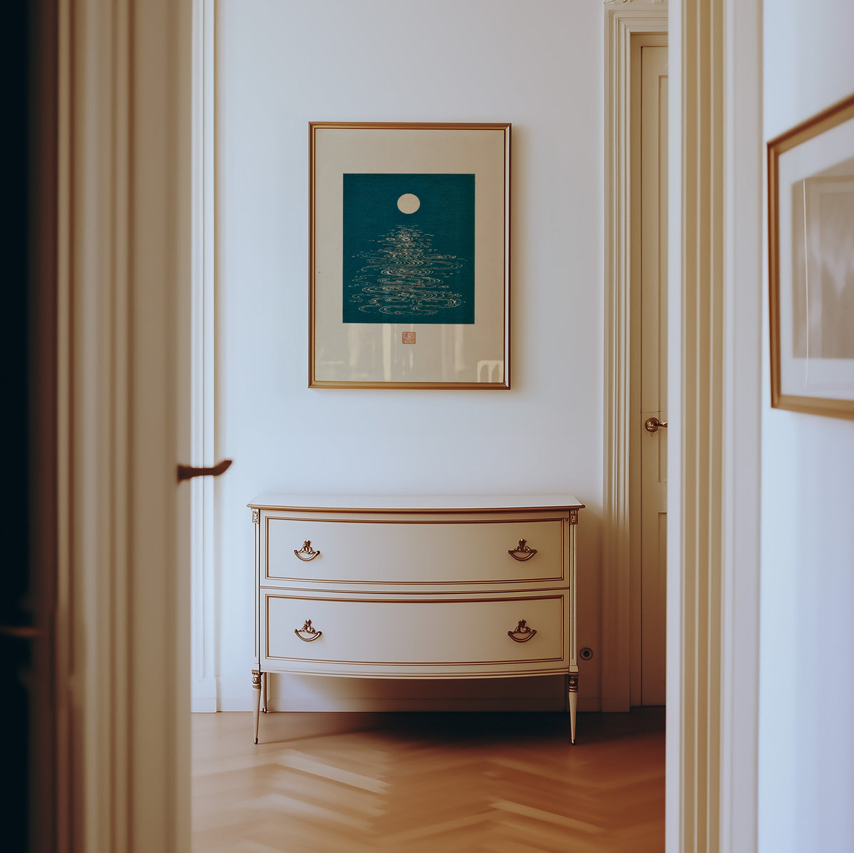 full moon over teal water print shown in a gold frame in a hallway above a cream dresser
