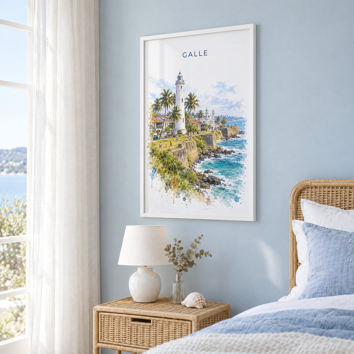 Galle, Sri Lanka watercolor print in a white frame on a pale blue wall beside a rattan bed in a coastal bedroom