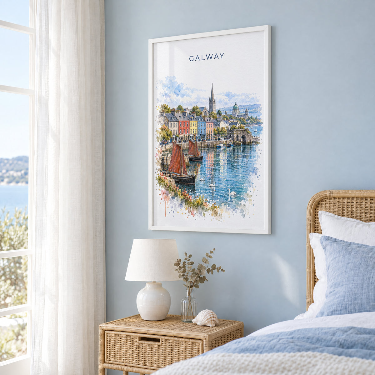 Galway watercolor print in a white frame on a pale blue wall beside a rattan bed in a coastal bedroom