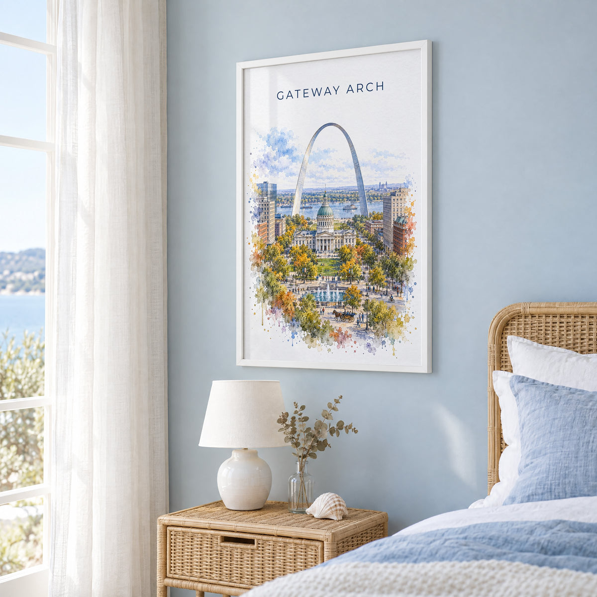 Gateway Arch National Park watercolor print in a white frame on a pale blue wall beside a rattan bed in a coastal bedroom