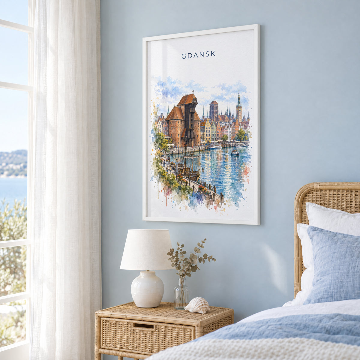 Gdansk watercolor print in a white frame on a pale blue wall beside a rattan bed in a coastal bedroom