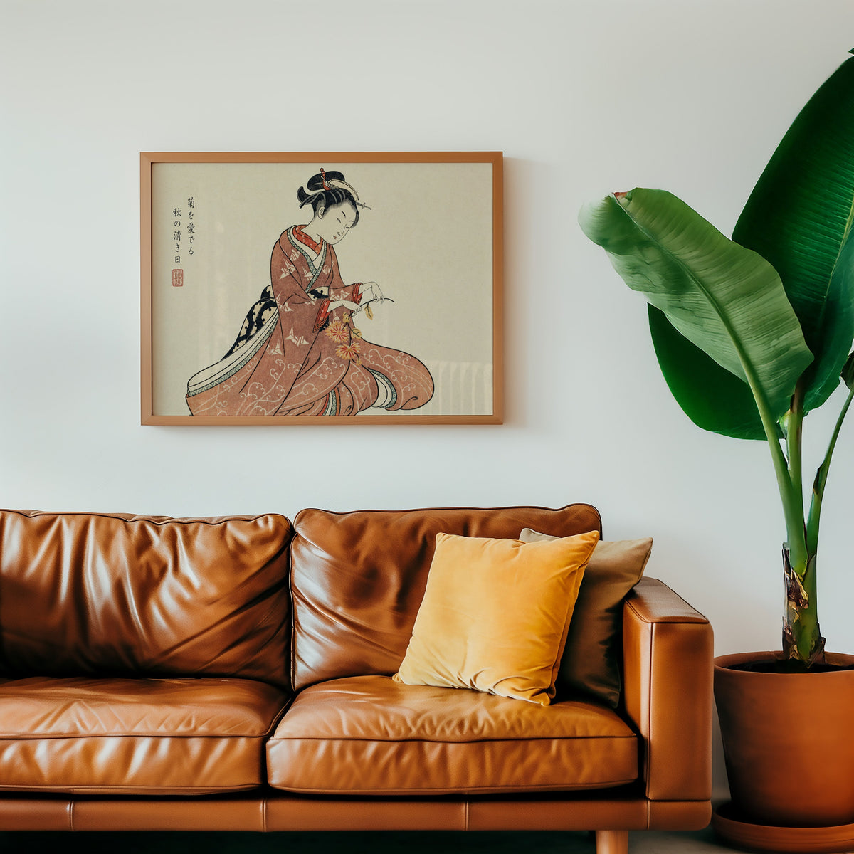 Kimono woman holding chrysanthemums print in a warm oak frame above a cognac leather sofa with a mustard pillow