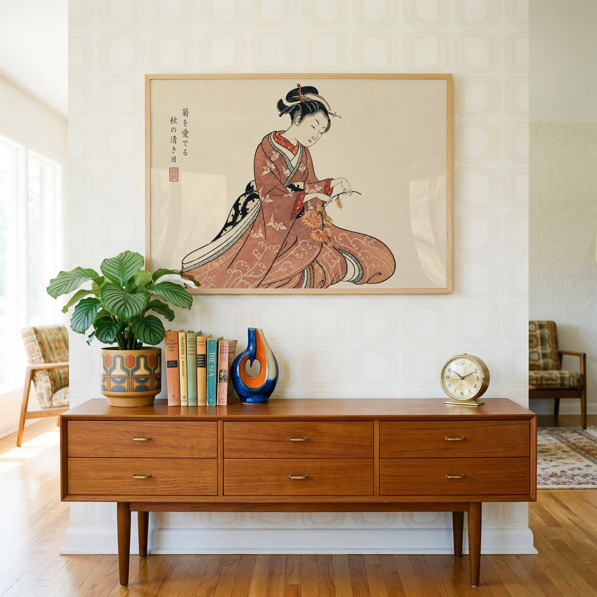 Kimono woman holding chrysanthemums print in a light oak frame above a teak credenza with books and a brass clock