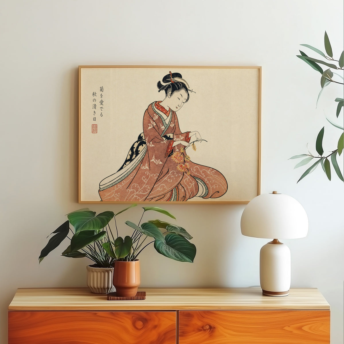 Kimono woman holding chrysanthemums print in a light oak frame above a wood sideboard with a white dome lamp
