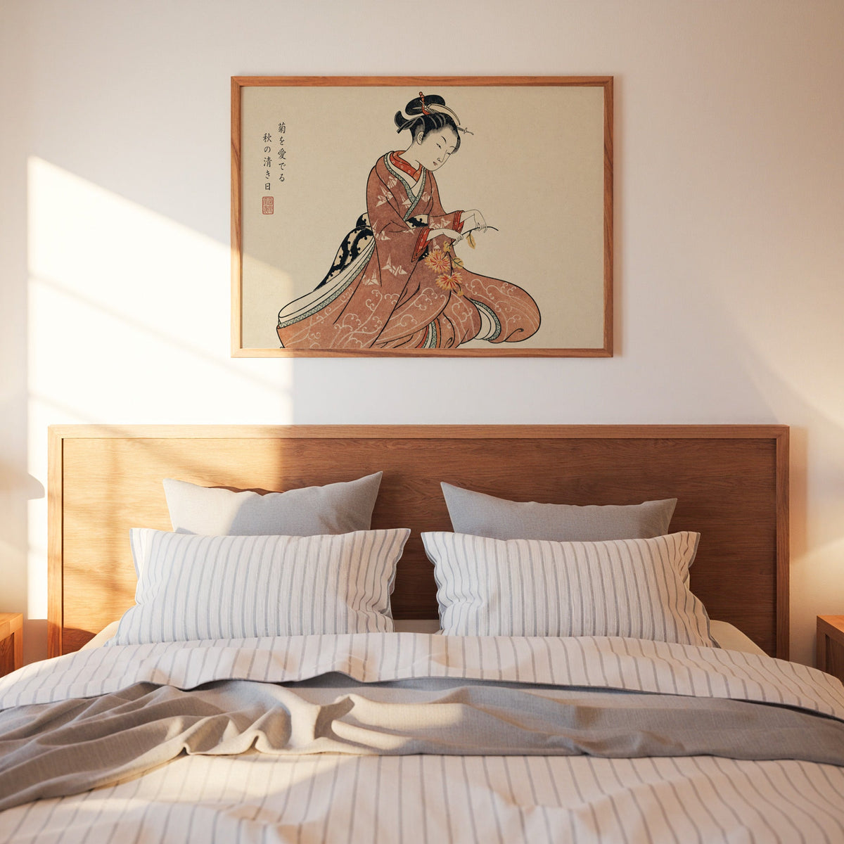 Kimono woman holding chrysanthemums print in a warm wood frame above a bed with striped linen bedding