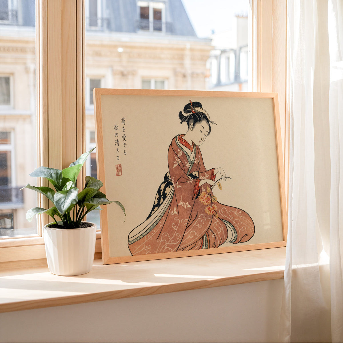 Kimono woman holding chrysanthemums print in a light wood frame leaning on a sunny windowsill by sheer curtains