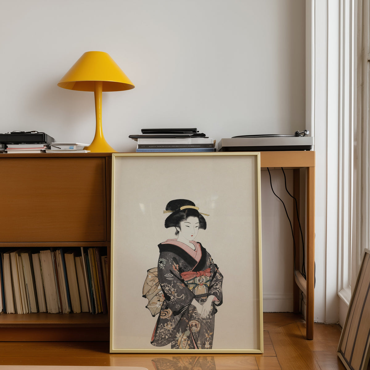 woman in dark floral kimono print shown in a gold frame leaning under a teak desk with a yellow lamp