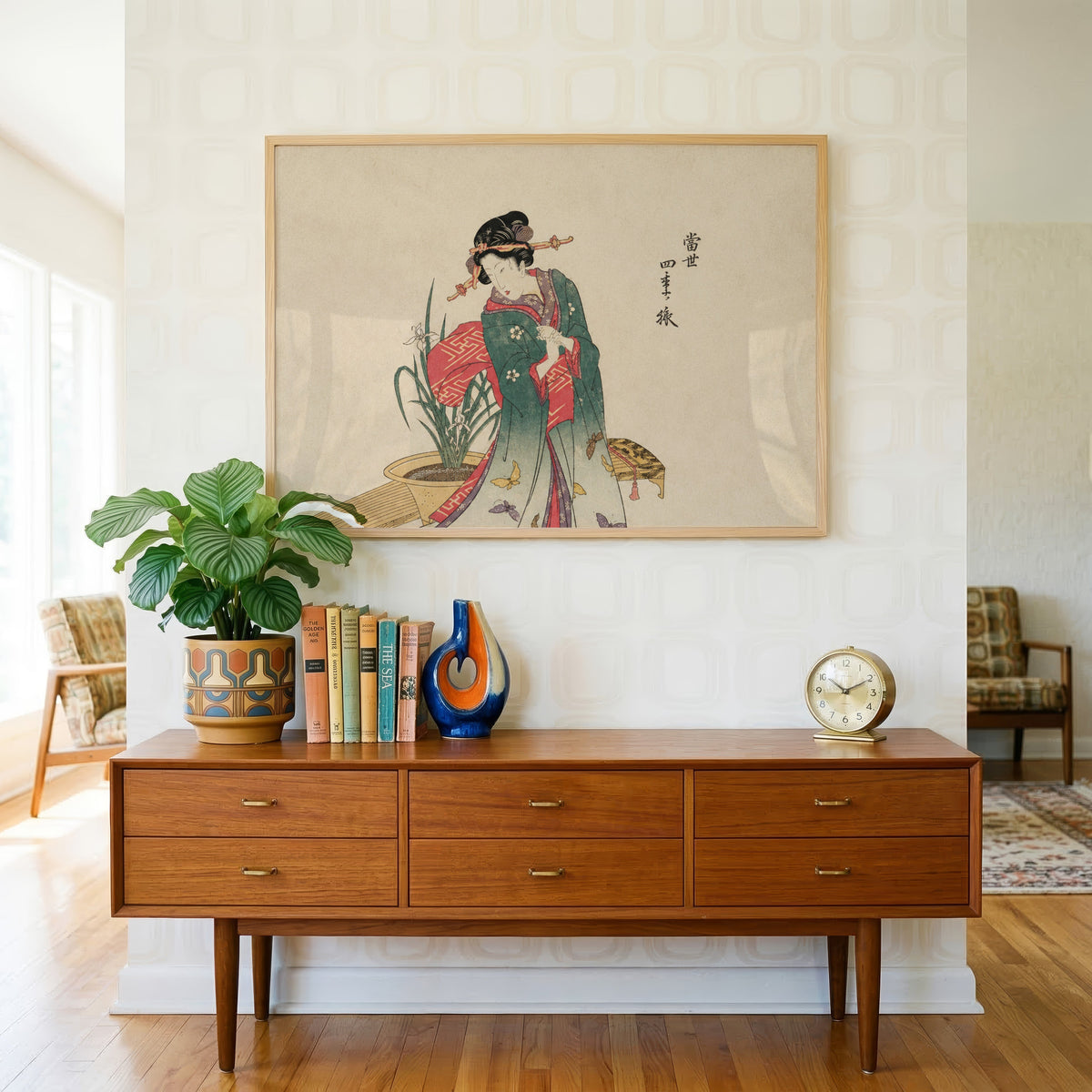 Woman in green kimono with butterflies print in a light oak frame above a teak credenza with books and a brass clock