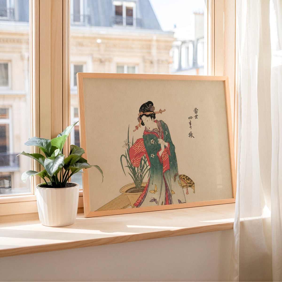 Woman in green kimono with butterflies print in a light wood frame leaning on a sunny windowsill by sheer curtains