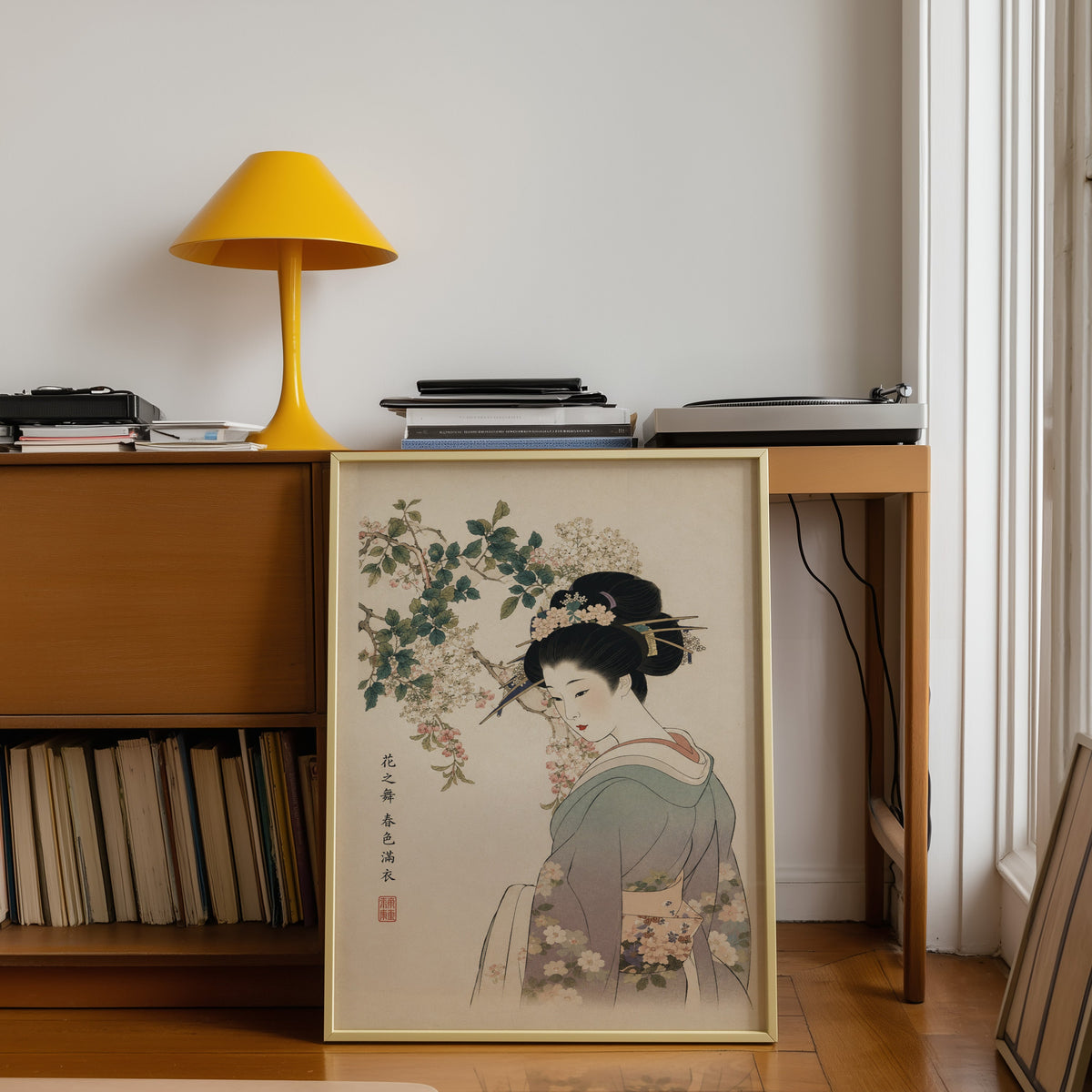 woman in lilac kimono under blossoms print shown in a gold frame leaning under a teak desk with a yellow lamp
