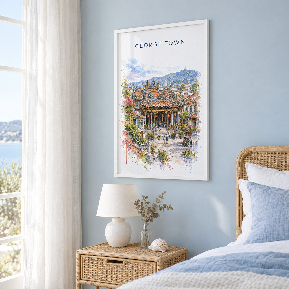 George Town, Malaysia watercolor print in a white frame on a pale blue wall beside a rattan bed in a coastal bedroom