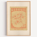 Georgia state flower stamp print in soft orange on wheat, light oak frame on a plain white wall